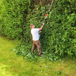 Ein Foto vom Inhaber mit einer Heckenschere beim Schneiden einer Hecke.